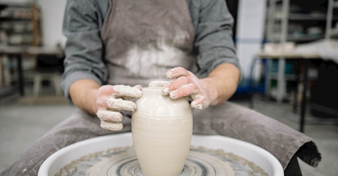 Closeup af kursist som drejer vase af ler på drejeskive