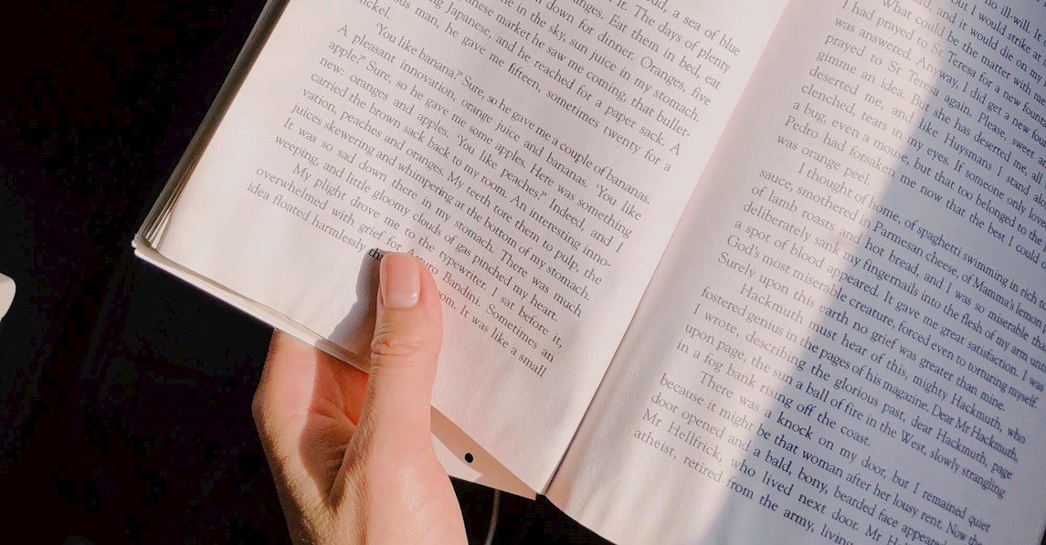 Closeup af kvindelig kursist som læser en paperback roman