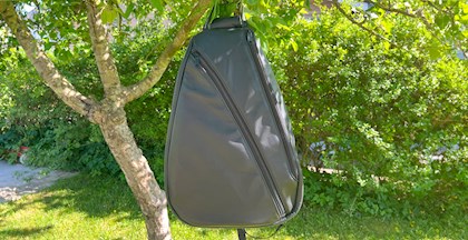 Hjemmelavet sort læder rygsæk/skuldertaske, der hænger i et træ i en solrig have (lavet af Inge Ryborg Lund)