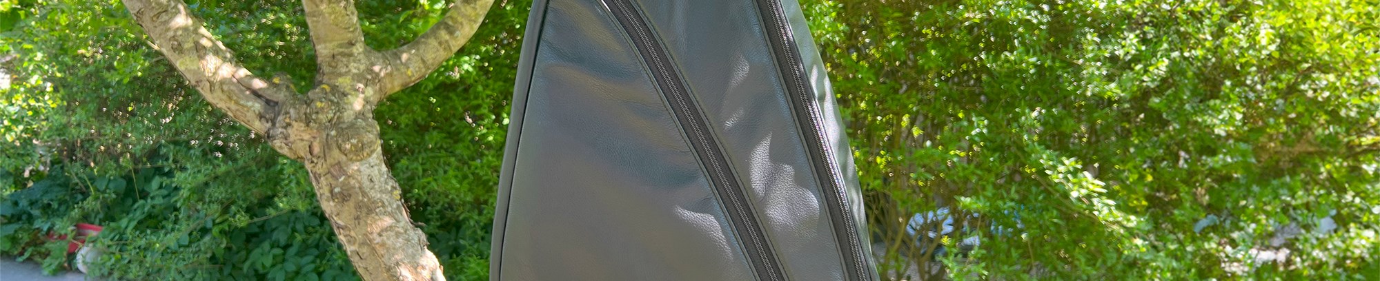 Hjemmelavet sort læder rygsæk/skuldertaske, der hænger i et træ i en solrig have (lavet af Inge Ryborg Lund)