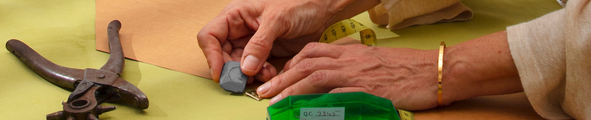 Kursist, der tegner en stencil/skabelon op på et stykke stof ved siden af en kasse med nåle, målebånd, saks, osv. på et bord