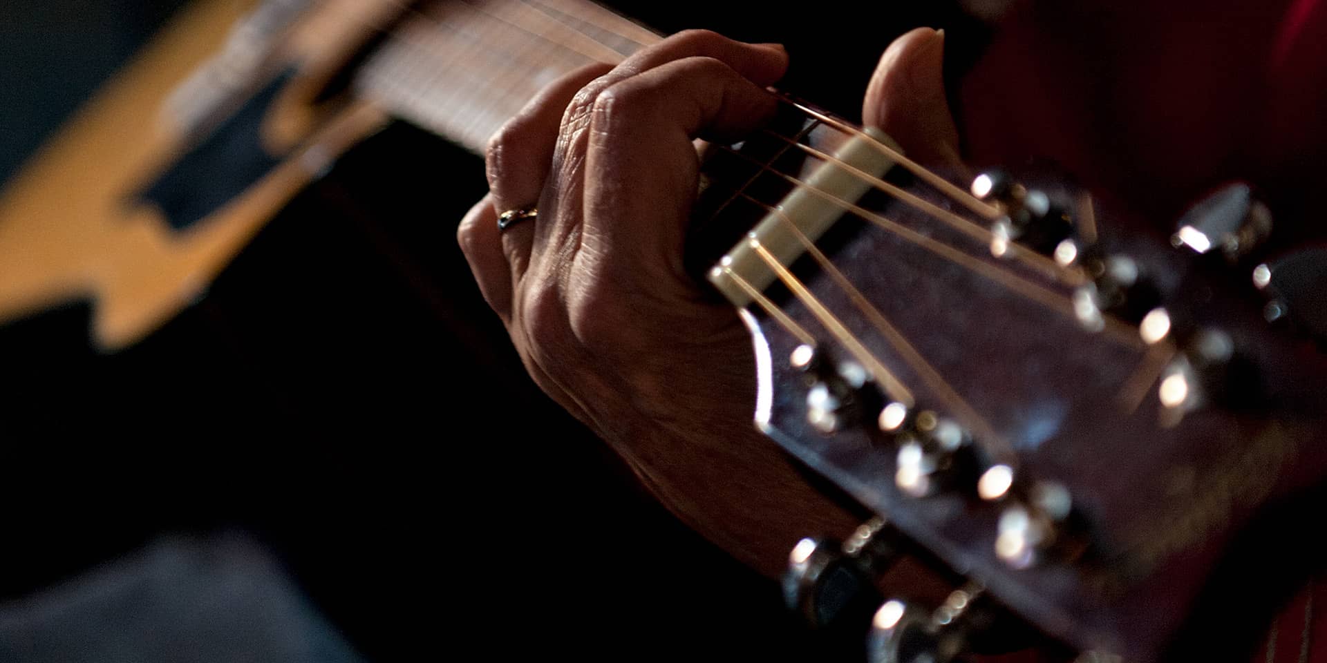 Man kan se en hånd, der holder om en guitar, og fingrene spiller på strengene. Fra et kursus i guitar i FOF Aarhus for begyndere og letøvede.